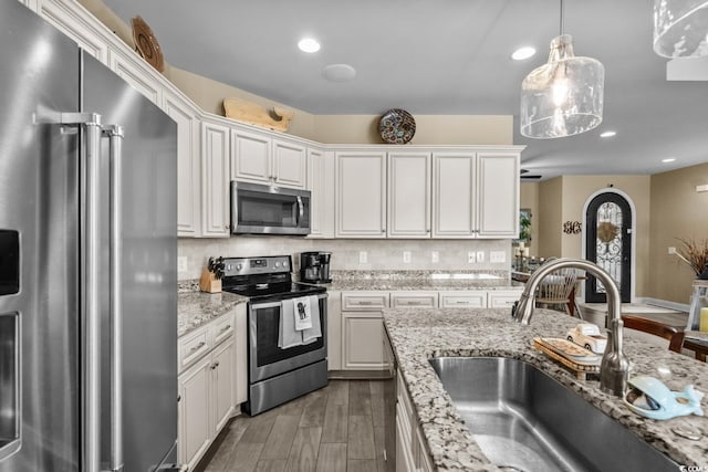 kitchen with stainless steel appliances, a sink, wood finished floors, white cabinets, and hanging light fixtures