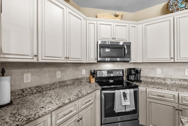kitchen featuring appliances with stainless steel finishes, white cabinetry, tasteful backsplash, and light stone countertops