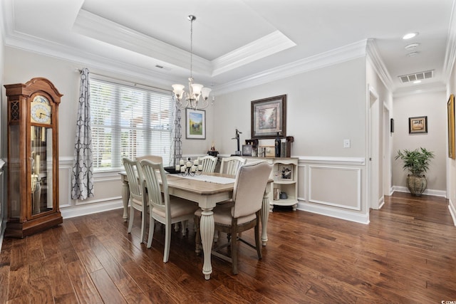 dining space with a chandelier, dark wood-style flooring, crown molding, a tray ceiling, and wainscoting