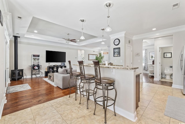 kitchen with ceiling fan, light tile patterned floors, crown molding, light stone countertops, and a breakfast bar area
