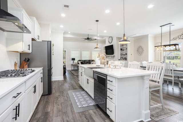 kitchen with dishwasher, wall chimney exhaust hood, open floor plan, a ceiling fan, and a breakfast bar