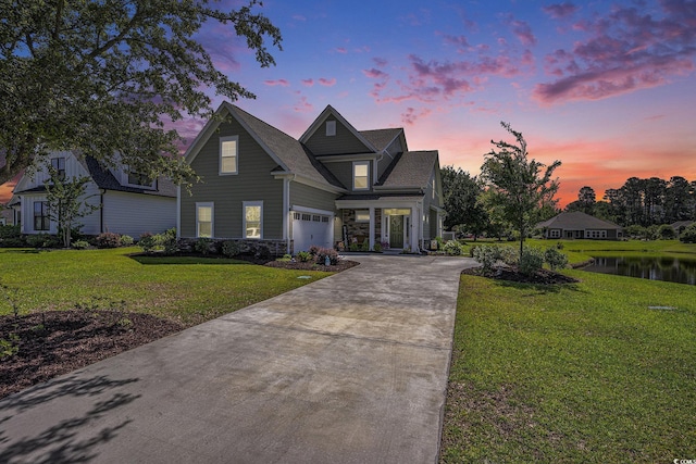 view of front of home with driveway, a lawn, a water view, and stone siding