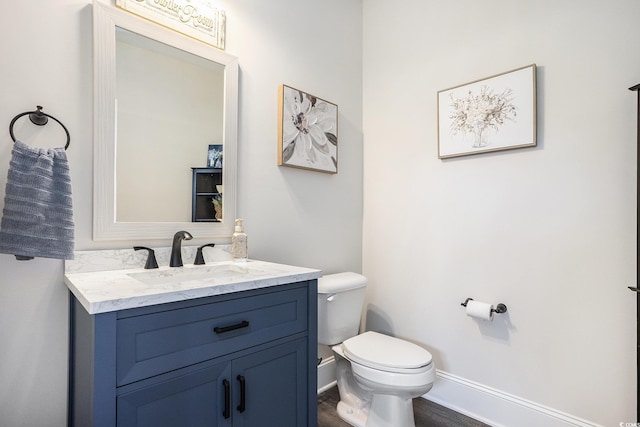 half bath with toilet, vanity, wood finished floors, and baseboards