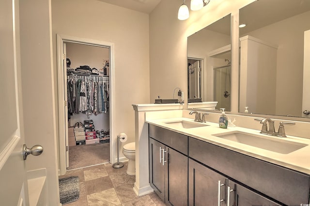 full bathroom with a stall shower, toilet, double vanity, a walk in closet, and baseboards