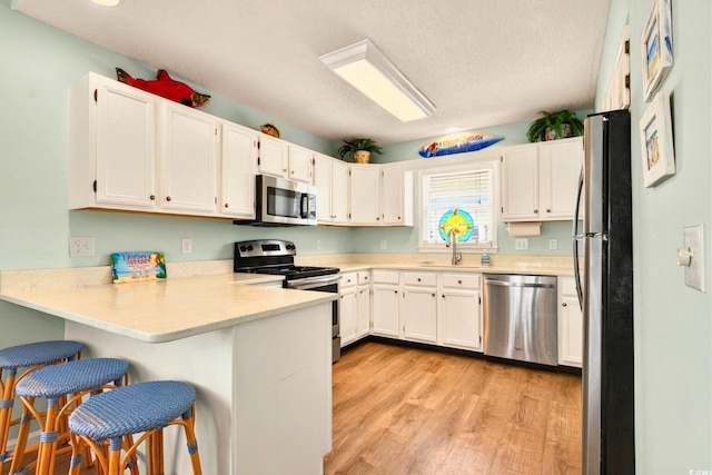 6 Indigo Ct, Ocean Isle Beach, NC 28469 - kitchen with stainless steel appliances, a peninsula, light wood-style flooring, light countertops, and white cabinets