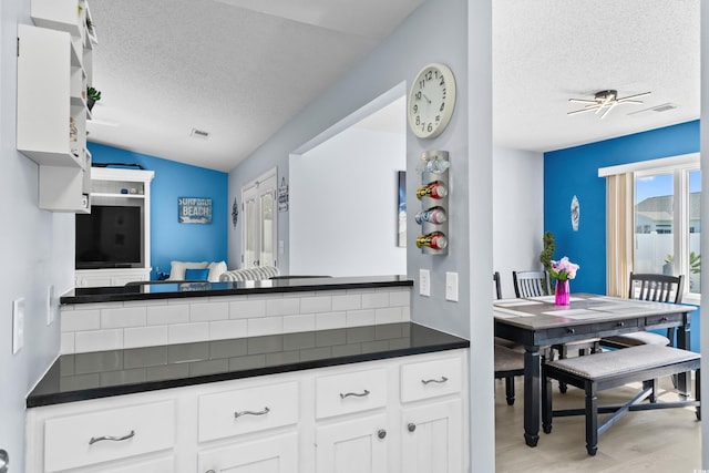 502 Garden Dr, Surfside Beach, SC 29575 - kitchen with a textured ceiling, dark countertops, vaulted ceiling, light wood-type flooring, and white cabinets