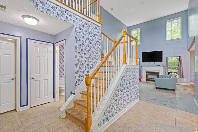 1033 Mccall Loop, Conway, SC 29526 - tiled foyer entrance featuring stairway, baseboards, a glass covered fireplace, wallpapered walls, and a textured ceiling
