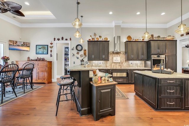 81 Cascade Dr, Murrells Inlet, SC 29576 - kitchen featuring wall chimney exhaust hood, a ceiling fan, a kitchen breakfast bar, decorative backsplash, and pendant lighting