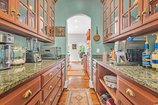 2382 Waverly Rd, Pawleys Island, SC 29585 - kitchen featuring light wood finished floors, arched walkways, brown cabinets, light stone countertops, and glass insert cabinets