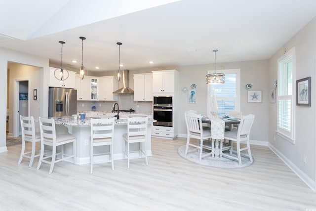 383 Mikita Dr, Surfside Beach, SC 29575 - kitchen with appliances with stainless steel finishes, wall chimney range hood, light wood-style floors, backsplash, and white cabinetry