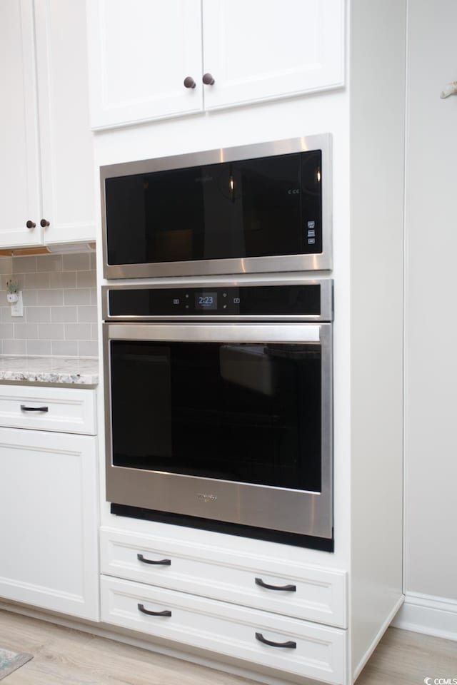 383 Mikita Dr, Surfside Beach, SC 29575 - kitchen featuring appliances with stainless steel finishes, light stone counters, decorative backsplash, white cabinets, and light wood finished floors