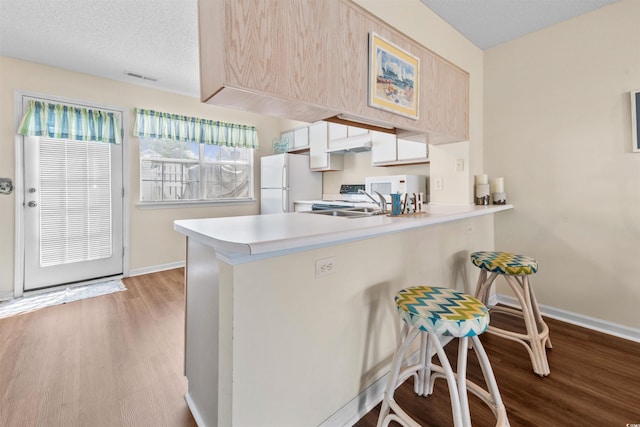 613 S 2nd Ave Unit 21D, North Myrtle Beach, SC 29582 - kitchen with white appliances, light countertops, wood finished floors, a peninsula, and a breakfast bar area