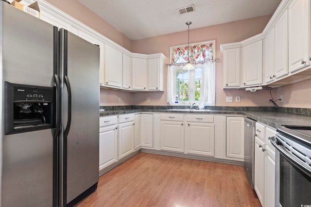 618 5th Ave S, North Myrtle Beach, SC 29582 - kitchen with stainless steel appliances, white cabinets, dark countertops, a sink, and light wood-type flooring