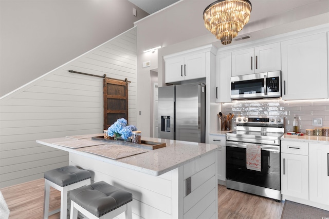 210 Double Eagle Dr Unit B-2, Surfside Beach, SC 29575 - kitchen with appliances with stainless steel finishes, a barn door, a center island, white cabinetry, and light stone counters