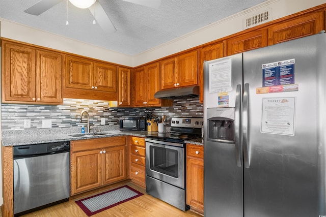 6309 N Ocean Blvd Unit 14E, North Myrtle Beach, SC 29582 - kitchen featuring appliances with stainless steel finishes, under cabinet range hood, a sink, brown cabinetry, and stone countertops