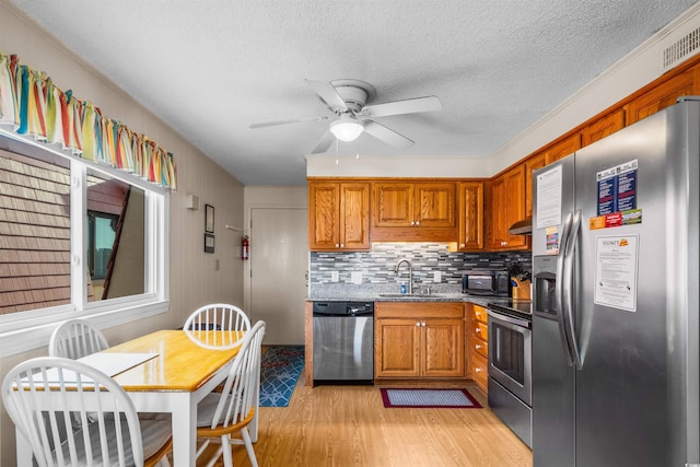 6309 N Ocean Blvd Unit 14E, North Myrtle Beach, SC 29582 - kitchen with appliances with stainless steel finishes, a sink, under cabinet range hood, light wood-style floors, and brown cabinets