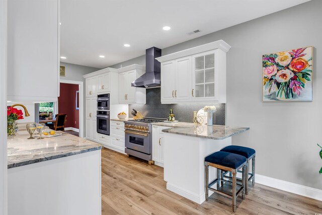 2150 N Berwick Dr, Myrtle Beach, SC 29575 - kitchen with stainless steel appliances, wall chimney range hood, a peninsula, light wood finished floors, and white cabinetry