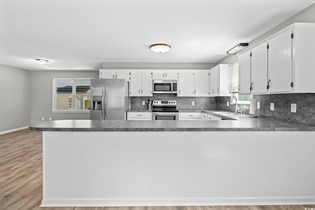 204 Elm St, Johnsonville, SC 29555 - kitchen with appliances with stainless steel finishes, decorative backsplash, a textured ceiling, light wood-style flooring, and a peninsula