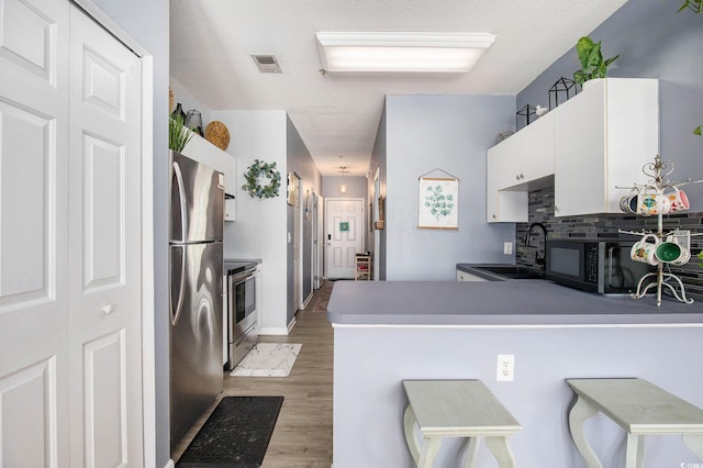 3939 Gladiola Ct Unit 202, Myrtle Beach, SC 29588 - kitchen with appliances with stainless steel finishes, a sink, white cabinetry, light wood-style floors, and a peninsula