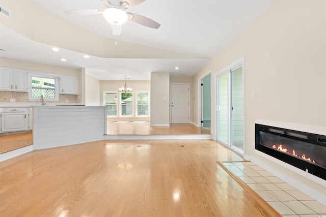 814 Night Heron Ln, Myrtle Beach, SC 29572 - unfurnished living room with light wood-style floors, a glass covered fireplace, a chandelier, vaulted ceiling, and ceiling fan