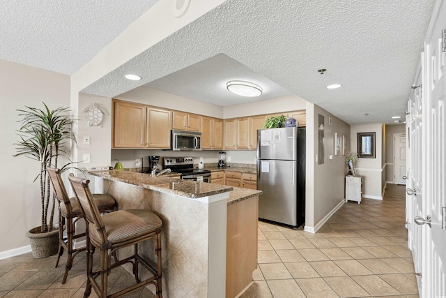 1625 S Ocean Blvd Unit 309, North Myrtle Beach, SC 29582 - kitchen featuring appliances with stainless steel finishes, light brown cabinetry, a peninsula, a textured ceiling, and baseboards