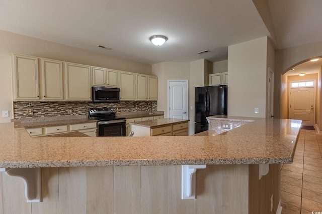 1224 Checkerberry St, Longs, SC 29568 - kitchen featuring black appliances, arched walkways, cream cabinetry, backsplash, and light tile patterned floors