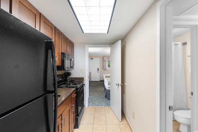1105 S Ocean Blvd Unit 110, Myrtle Beach, SC 29577 - kitchen featuring black appliances, brown cabinets, light tile patterned floors, dark stone countertops, and a drop ceiling