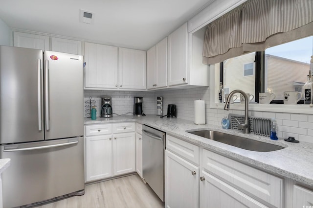 4307 Beverly Ct, North Myrtle Beach, SC 29582 - kitchen featuring appliances with stainless steel finishes, a sink, decorative backsplash, white cabinets, and light wood-type flooring