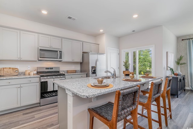 2889 Riverboat Way, Conway, SC 29526 - kitchen with appliances with stainless steel finishes, a kitchen breakfast bar, light wood finished floors, a kitchen island with sink, and light stone counters