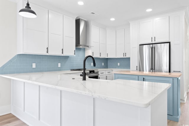 4617 Hedrick St, North Myrtle Beach, SC 29582 - kitchen with appliances with stainless steel finishes, wall chimney range hood, a peninsula, light wood-style floors, and backsplash