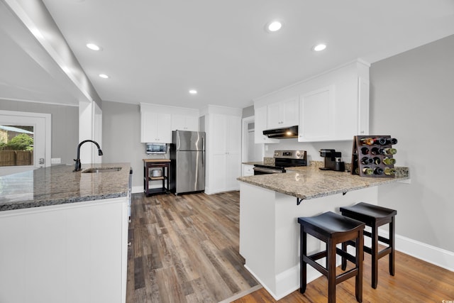 1155 Palmetto St, Georgetown, SC 29440 - kitchen featuring appliances with stainless steel finishes, under cabinet range hood, a peninsula, wood finished floors, and stone counters