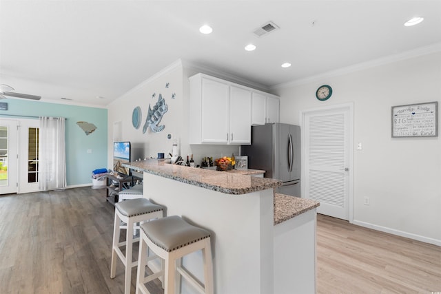 411 Mahogany Dr Unit 101, Murrells Inlet, SC 29576 - kitchen with freestanding refrigerator, a kitchen breakfast bar, crown molding, white cabinetry, and light wood-type flooring
