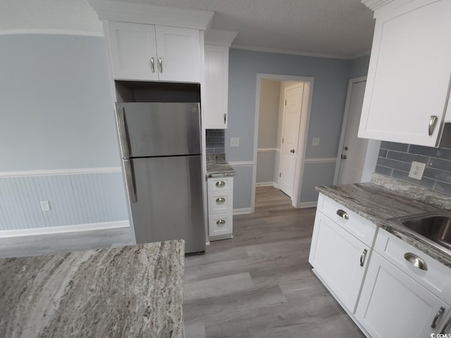 300 47th Ave S Unit 1F, North Myrtle Beach, SC 29582 - kitchen with freestanding refrigerator, white cabinetry, tasteful backsplash, light wood finished floors, and crown molding