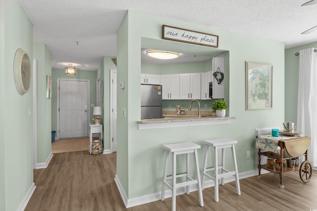 222 Landing Rd Unit 1811, North Myrtle Beach, SC 29582 - kitchen with freestanding refrigerator, wood finished floors, a kitchen bar, a textured ceiling, and white cabinets