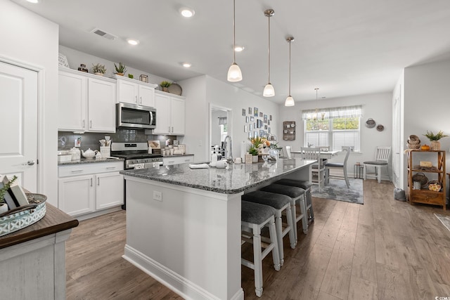 462 Pacific Commons Dr, Surfside Beach, SC 29575 - kitchen with stainless steel appliances, a center island with sink, wood finished floors, white cabinetry, and tasteful backsplash