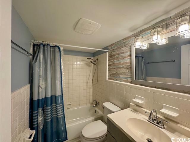 5409 N Ocean Blvd Unit 111, North Myrtle Beach, SC 29582 - bathroom featuring tile walls, shower / tub combo with curtain, vanity, toilet, and a wainscoted wall