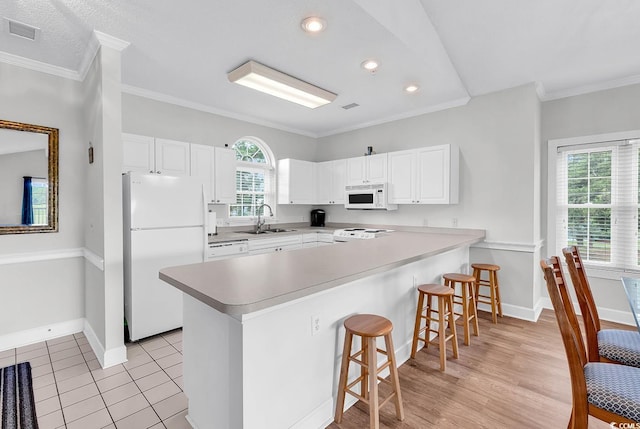 4811 Orchid Way Unit 301, Myrtle Beach, SC 29577 - kitchen with white appliances, a peninsula, a breakfast bar area, ornamental molding, and white cabinetry