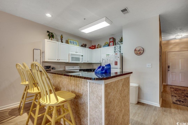 601 Hillside Dr N Unit 3704, North Myrtle Beach, SC 29582 - kitchen featuring white appliances, baseboards, light wood-type flooring, white cabinetry, and a kitchen breakfast bar