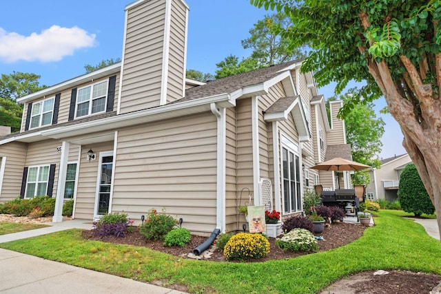 503 20th Ave N Unit 55B, North Myrtle Beach, SC 29582 - view of property exterior with a chimney, a shingled roof, and a yard