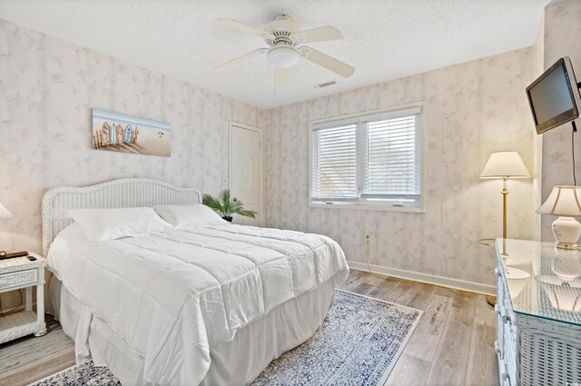 435 Ocean Creek Dr Unit 2722, Myrtle Beach, SC 29572 - bedroom with light wood-style floors, wallpapered walls, a textured ceiling, a ceiling fan, and baseboards