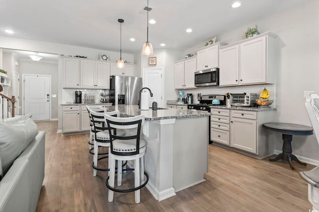 4927 Sandlewood Dr, Myrtle Beach, SC 29579 - kitchen featuring appliances with stainless steel finishes, decorative backsplash, light wood finished floors, a breakfast bar, and a kitchen island with sink