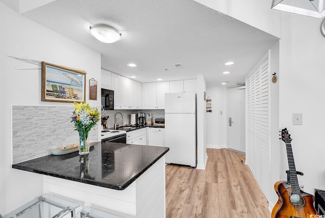 2501 S Ocean Blvd Unit 111, Myrtle Beach, SC 29577 - kitchen with freestanding refrigerator, black microwave, a peninsula, light wood-type flooring, and white cabinets