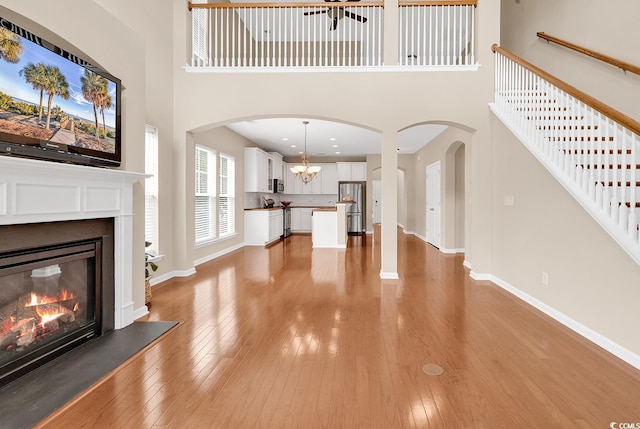 126 Dreamland Dr, Murrells Inlet, SC 29576 - unfurnished living room with a high ceiling, a glass covered fireplace, light wood-type flooring, baseboards, and stairs