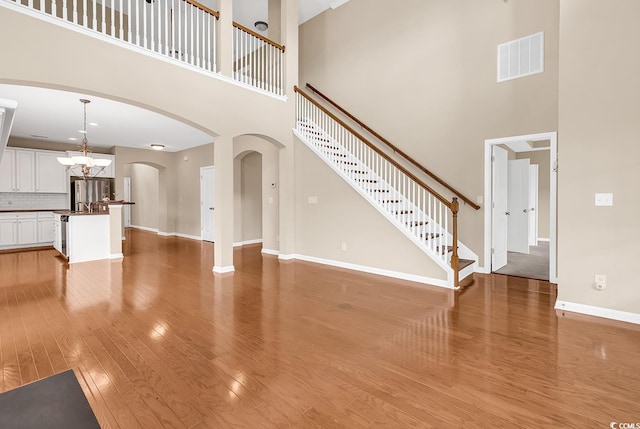126 Dreamland Dr, Murrells Inlet, SC 29576 - unfurnished living room featuring a towering ceiling, light wood-type flooring, baseboards, arched walkways, and stairs