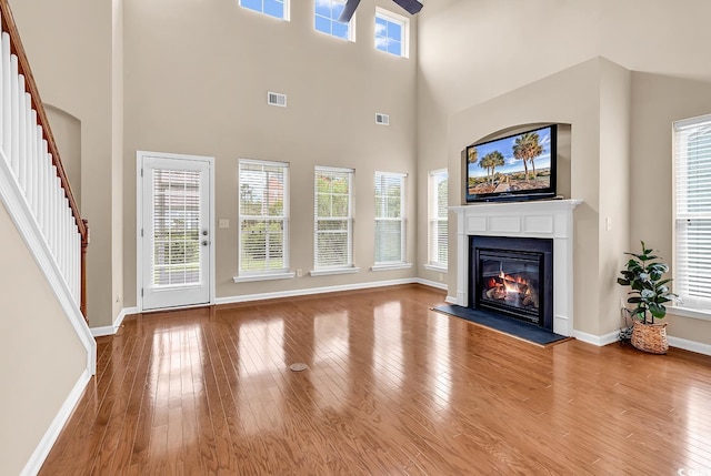 126 Dreamland Dr, Murrells Inlet, SC 29576 - unfurnished living room featuring a ceiling fan, a glass covered fireplace, stairs, wood finished floors, and a high ceiling