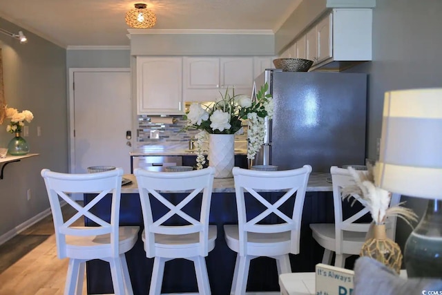 5601 N Ocean Blvd Unit A-307, Myrtle Beach, SC 29577 - kitchen featuring freestanding refrigerator, white cabinetry, ornamental molding, a kitchen bar, and light wood-style flooring