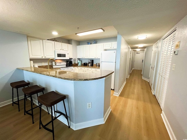 2007 S Ocean Blvd Unit 1506, Myrtle Beach, SC 29577 - kitchen with white appliances, light wood finished floors, a peninsula, a kitchen bar, and white cabinetry