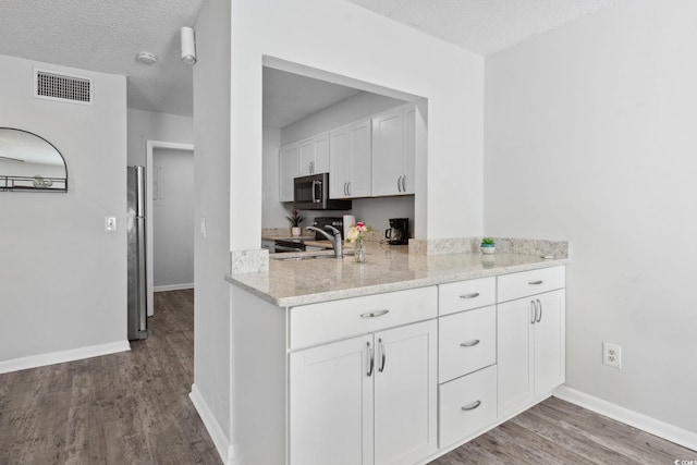 800 9th Ave S Unit E-4, North Myrtle Beach, SC 29582 - kitchen featuring wood finished floors, white cabinets, a textured ceiling, appliances with stainless steel finishes, and light stone counters