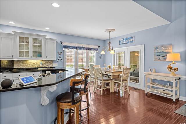 504 Sea Vista Ln, North Myrtle Beach, SC 29582 - kitchen featuring a breakfast bar area, glass insert cabinets, backsplash, dark wood-type flooring, and white cabinetry