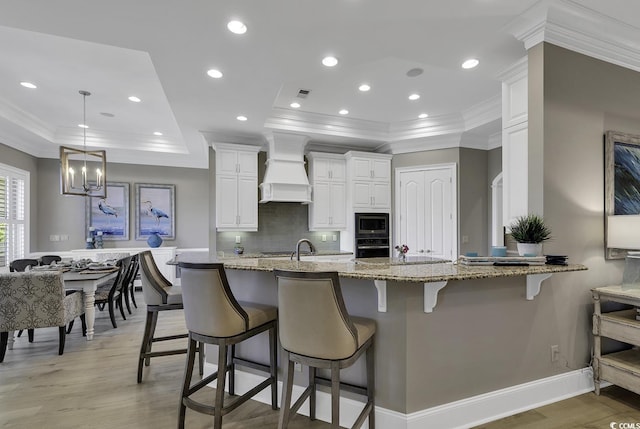 1108 Surf Pointe Dr, North Myrtle Beach, SC 29582 - kitchen with crown molding, custom range hood, built in microwave, white cabinetry, and a raised ceiling